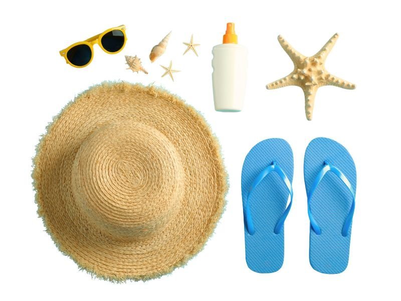Flat lay con oggetti da viaggio estivi: cappello da sole, occhiali, crema solare e accessori per vacanze al mare
